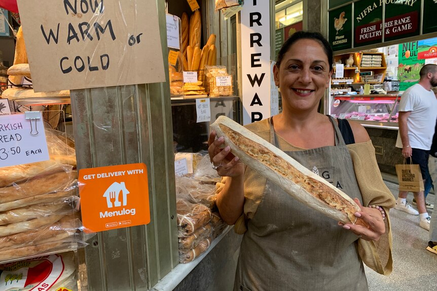 A woman holds a bread in front of a bakery.