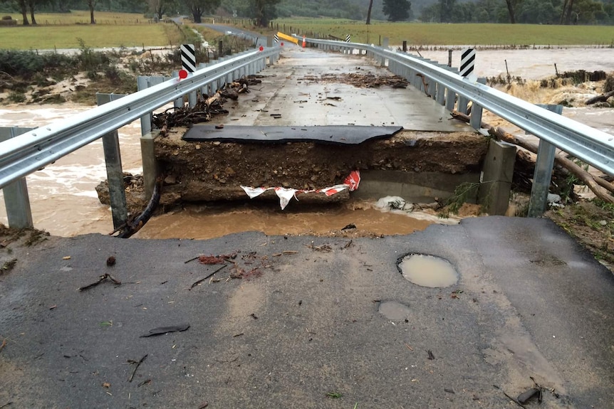 Eye level view of a large section of a low road bridge washed away, cutting the bridge in two.