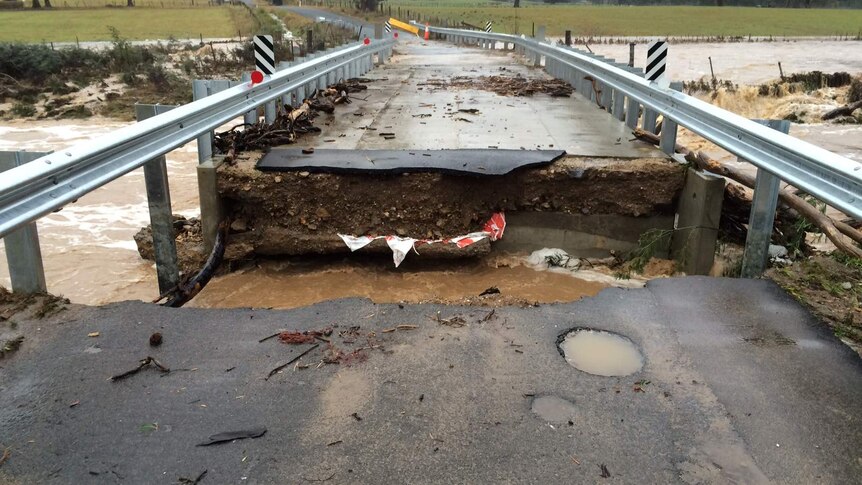Eye level view of a large section of a low road bridge washed away, cutting the bridge in two.
