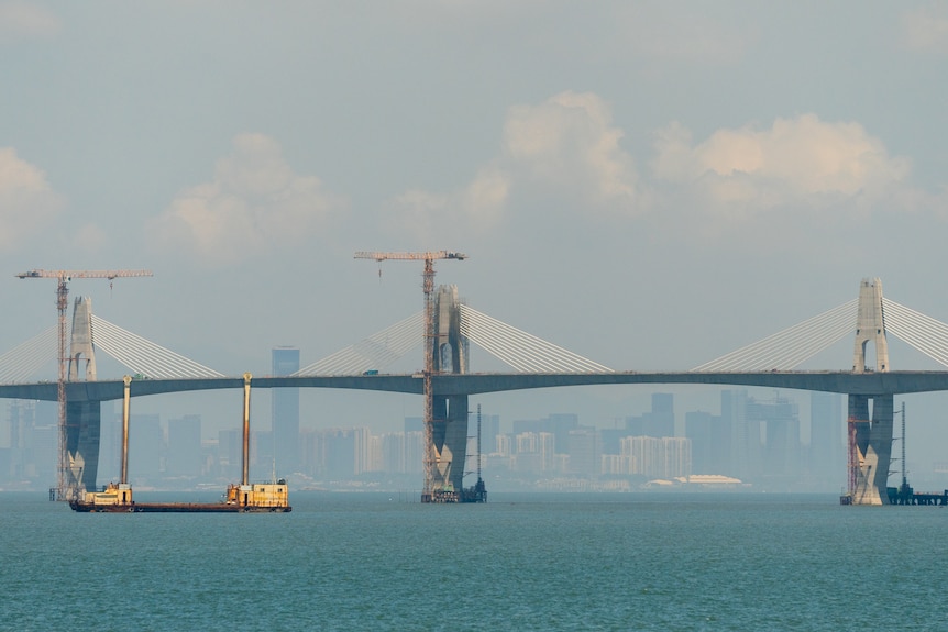 A boat passes under a bridge with a city in the background.