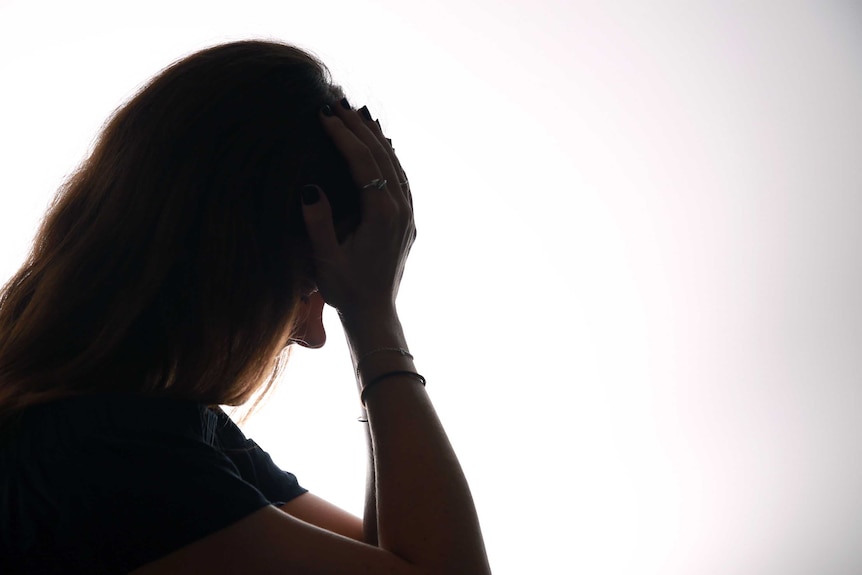 A silhouetted woman holds her head in her hands.