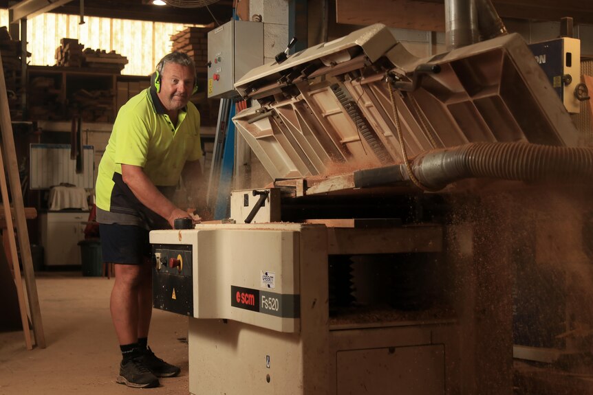 Peter Ayres puts a plank of timber through a machine with sawdust spraying out the top.