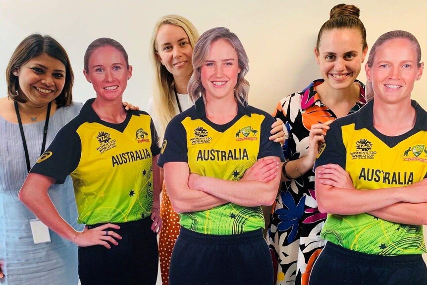 Rica and two other women (who host the podcast show) stand among life sized cardboard cut outs of the Australian cricket team