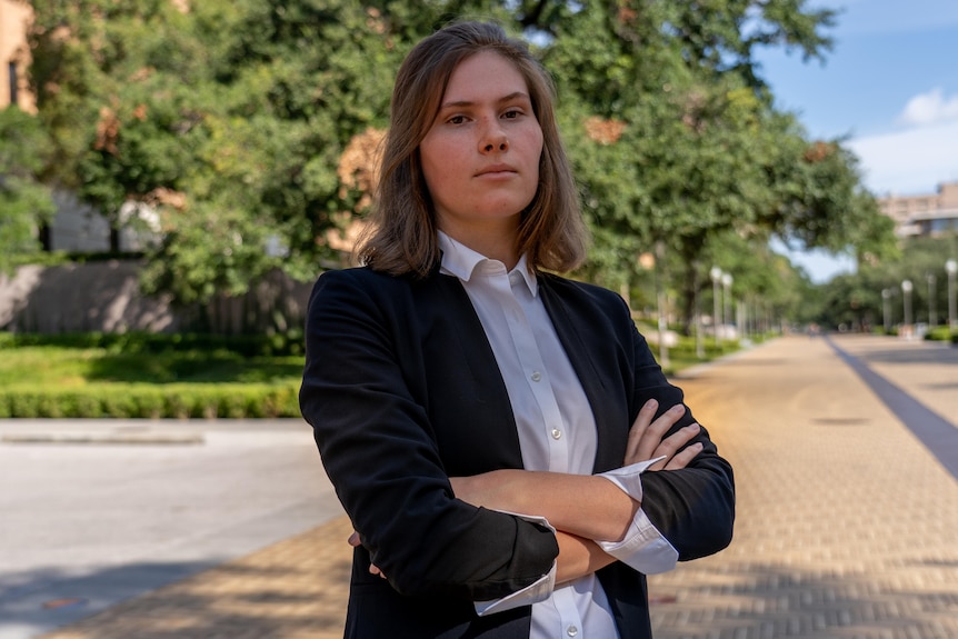 Woman in a white shirt and black blazer, standing with her arms folded.