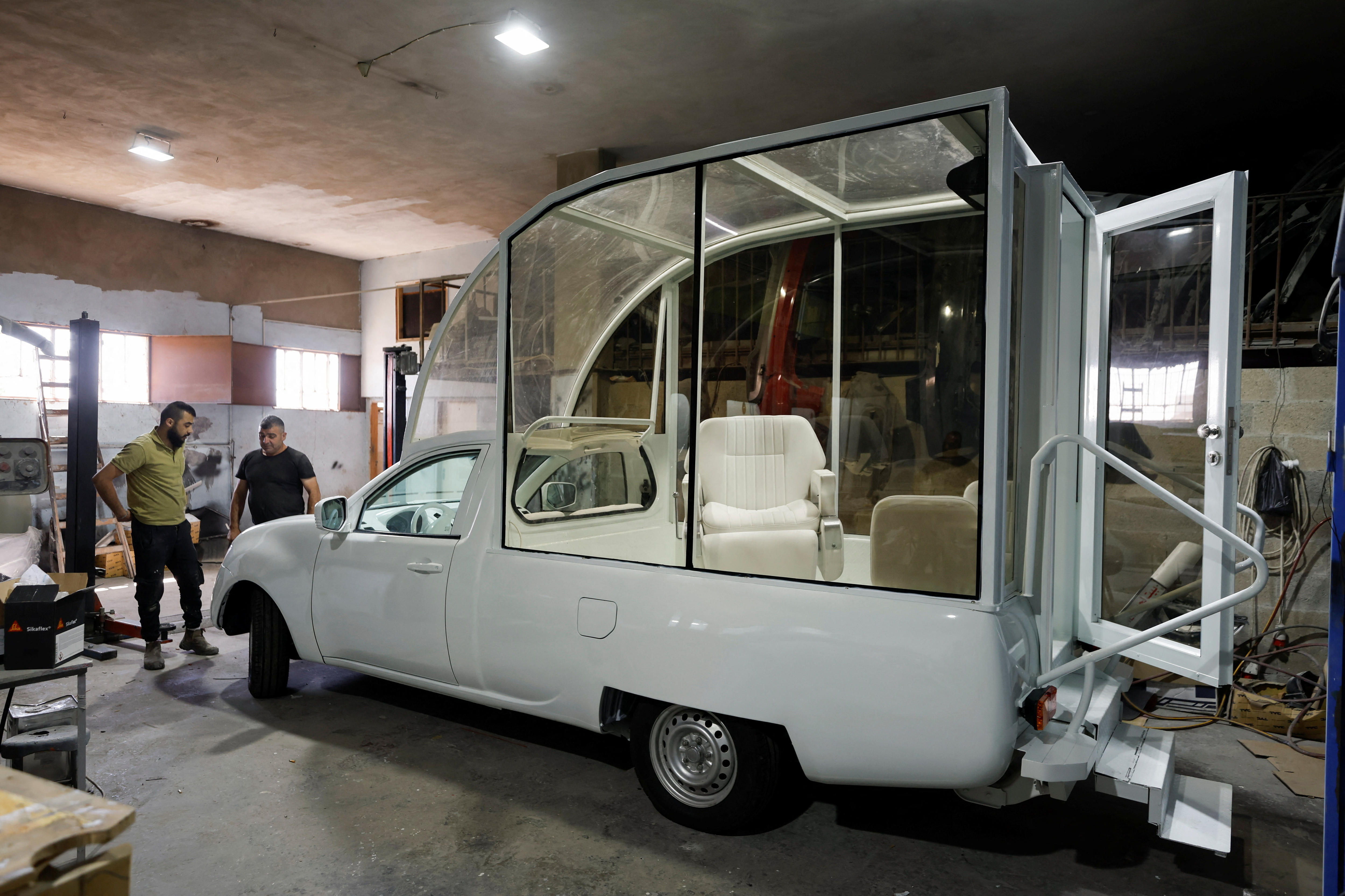 The truck in a car workshop nearly completed with the glass housing on the bed and two men standing in front of it