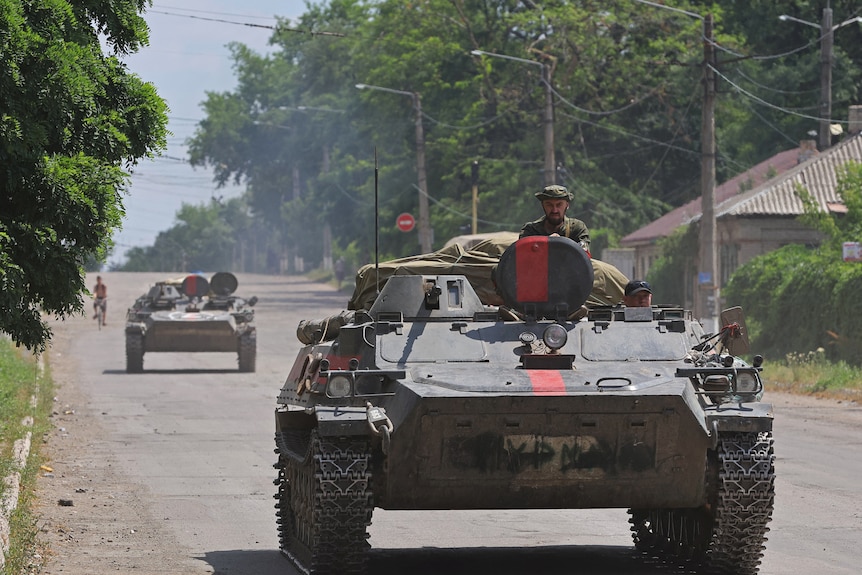 A man pokes his head out of a tank as it drives down a Ukrainian street.