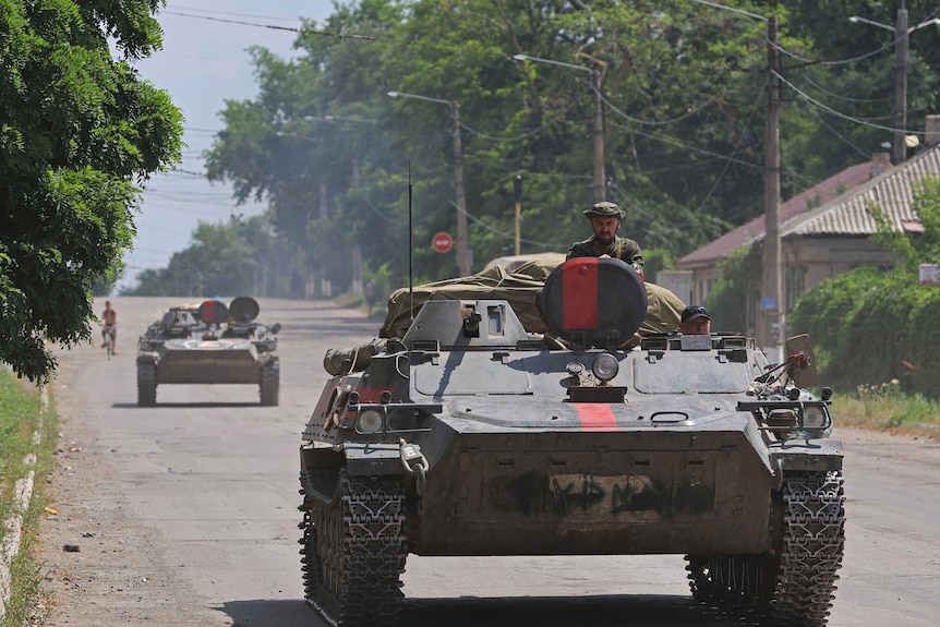 Man pokes head out of tank as it drives down a Ukrainian street