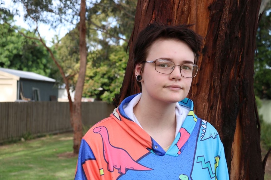 A young man with glasses stands outside wearing a colourful hoodie