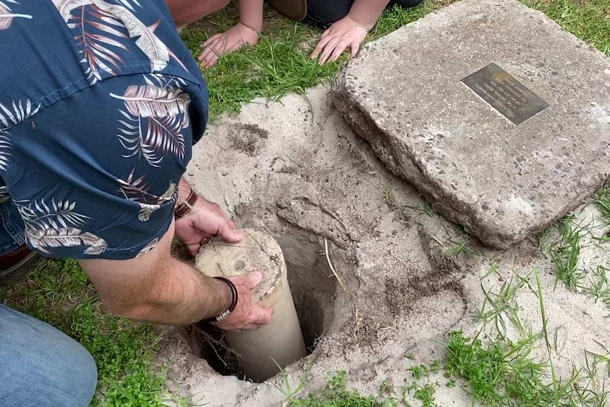 A man's hands lift a plastic tube out of the ground.