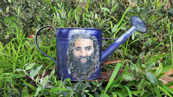 A blue metal watering can with a painted picture of Costa painted on it.