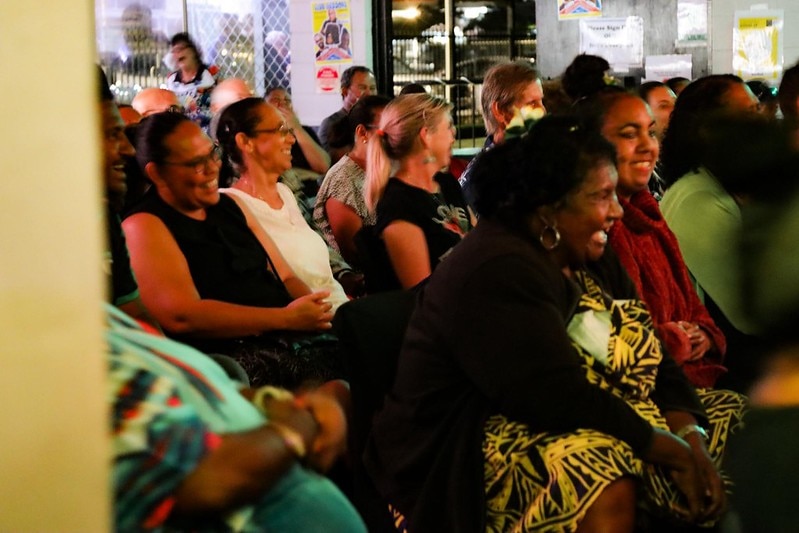 Four packed seated rows of Torres Strait Islanders looking toward a stage and laughing