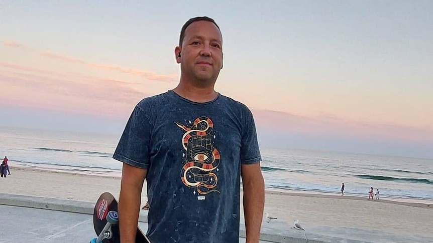 man in a t-shirt standing in front of a beach sunset
