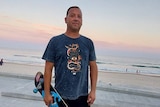 man in a t-shirt standing in front of a beach sunset