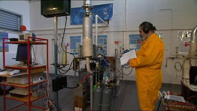 A man stands in a laboratory beside hydrogen bottles and other equipment