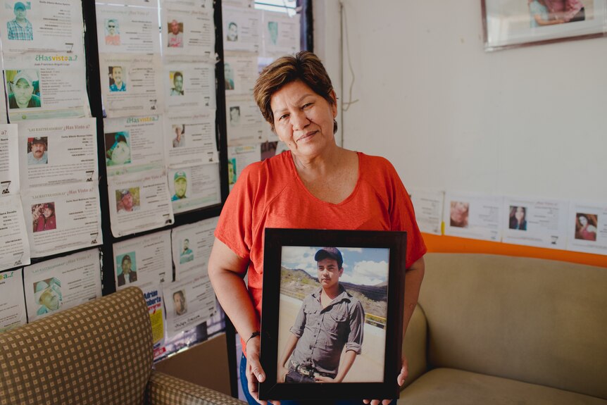 A woman holds a portrait of a young man.