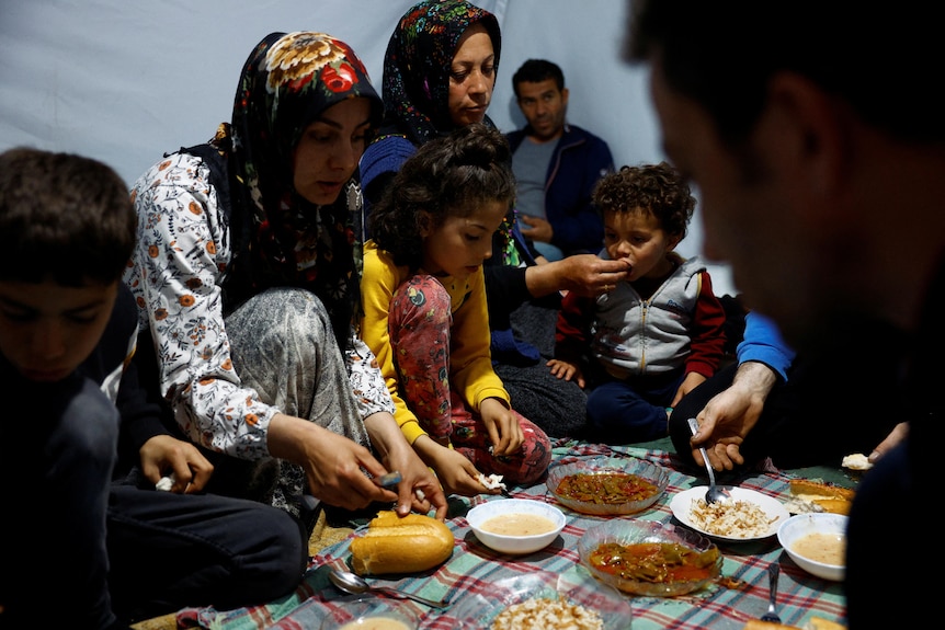 A woman and children surround bowls of food.
