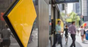 A Commonwealth Bank sign in the foreground with people blurred walking by in the background
