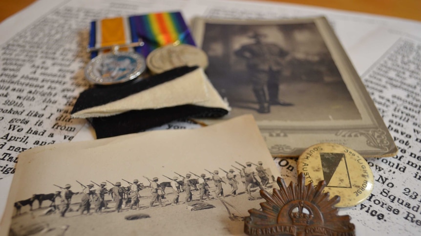 Some medals, old photographs and badges strewn across print-outs of a letter in a newspaper.