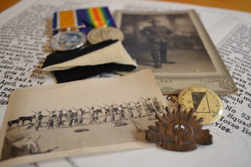 Some medals, old photographs and badges strewn across print-outs of a letter in a newspaper.