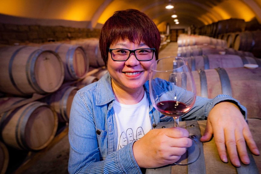 Wang Fang in a wine cellar with some red wine in a wine glass, ready to sample