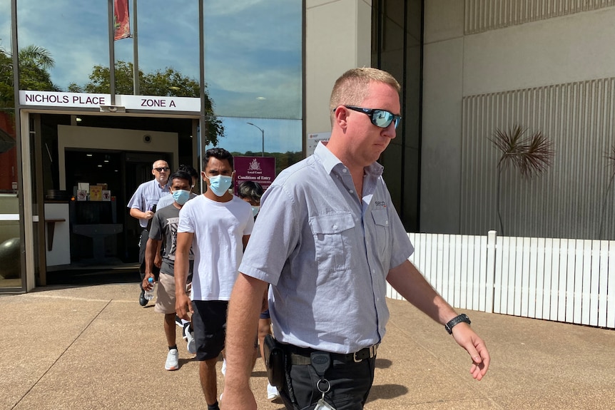 A group of people walking out of the Darwin Local Court building. 