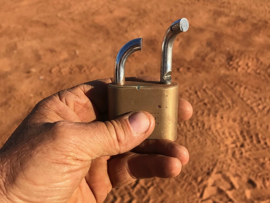 A man holds a broken padlock in his hand