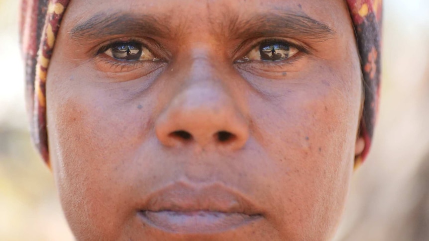 A close-up of an unsmiling indigenous woman looking directly at the camera.