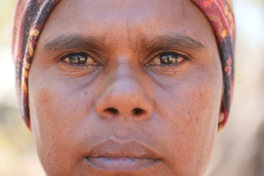 A close-up of an unsmiling indigenous woman looking directly at the camera.