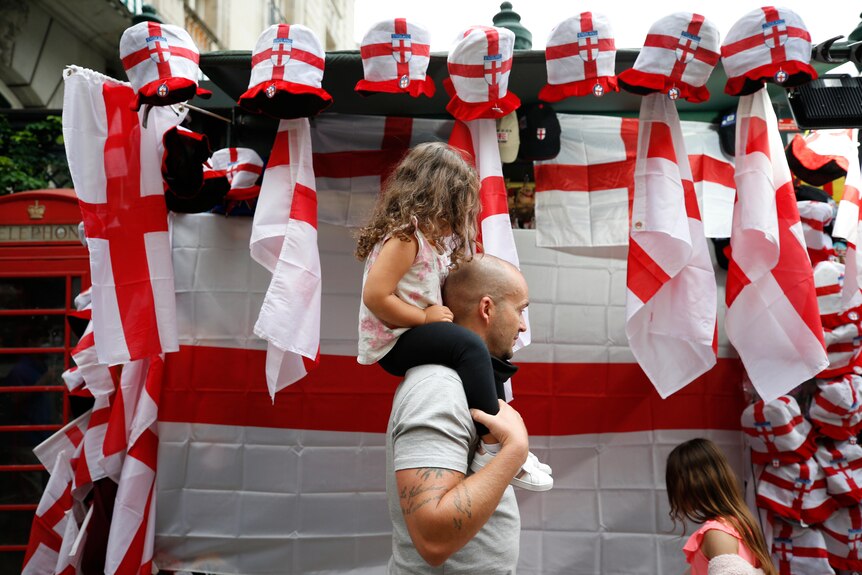 Man carries a child past England flags before a sports game