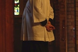 A priest stands in the corner of a church during a service.