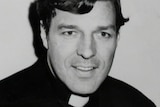 A black-and-white photograph of George Pell smiling in priest's attire.