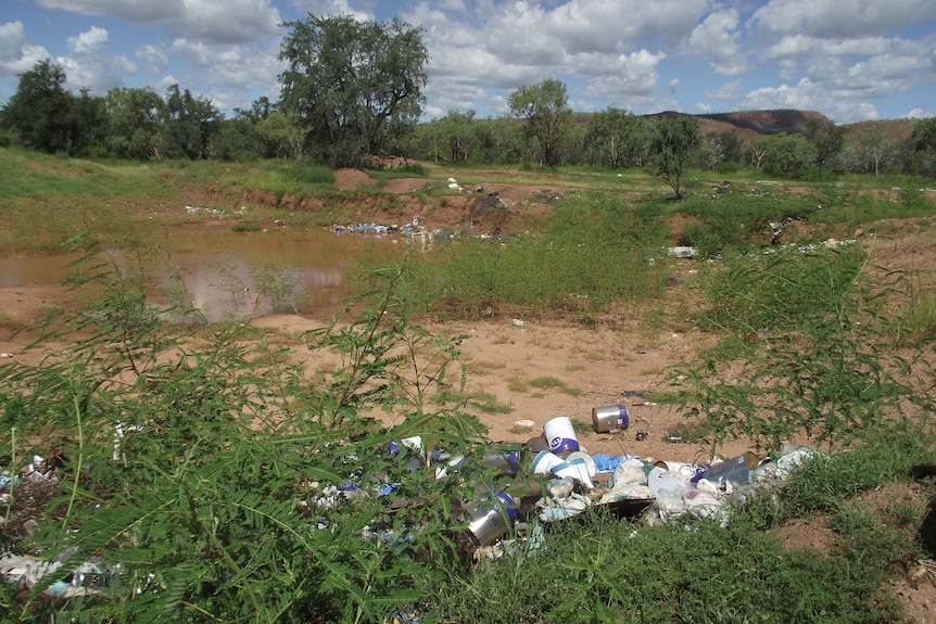 a pile of cans in front of a trench filled with brown water and rubbish