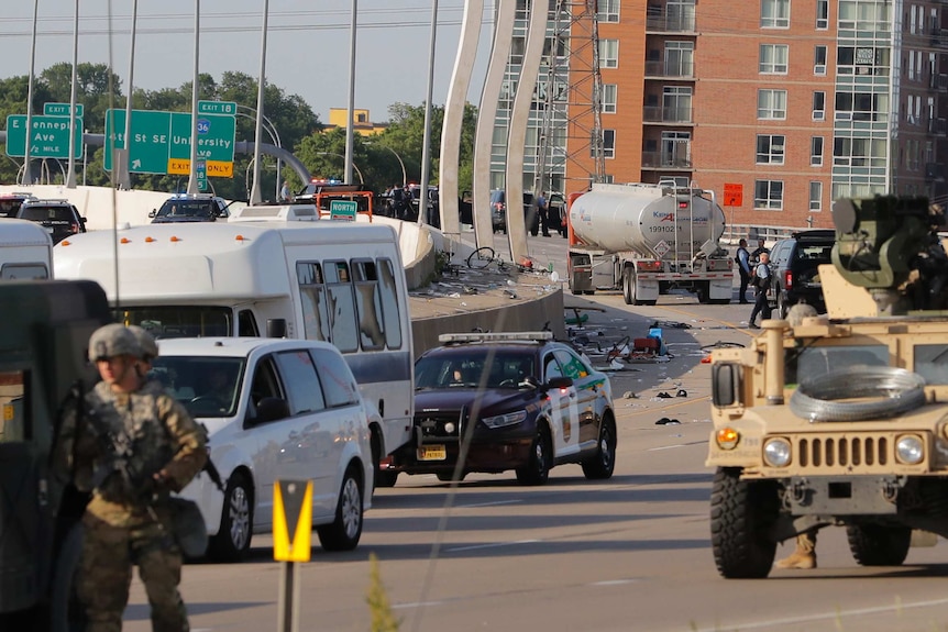 A large truck is surrounded by police and military vehicles on a freeway