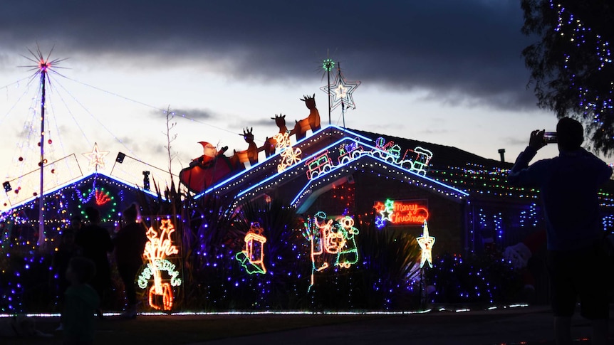 A man photographs a house covered in Christmas lights on his smartphone.
