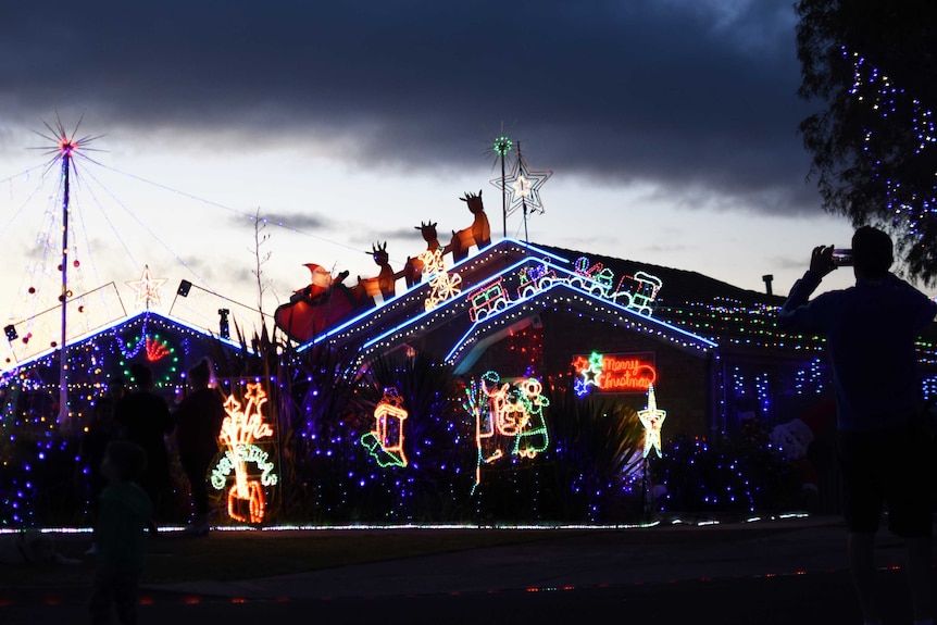 A man photographs a house covered in Christmas lights on his smartphone.