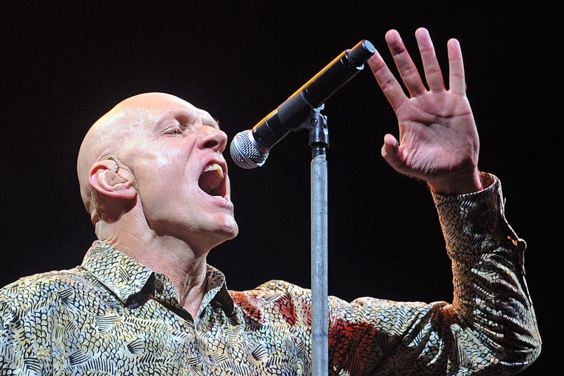 A tall, bald white man screams at a microphone.