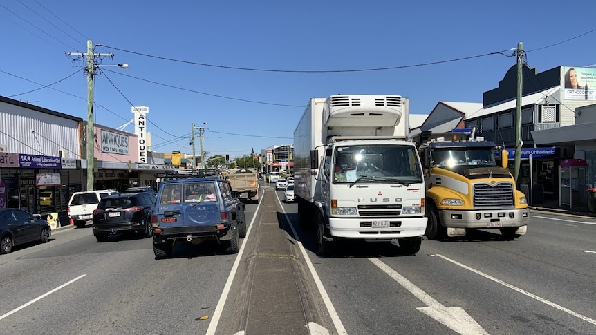 Traffic flows in both directions along a main road flanked by small businesses.