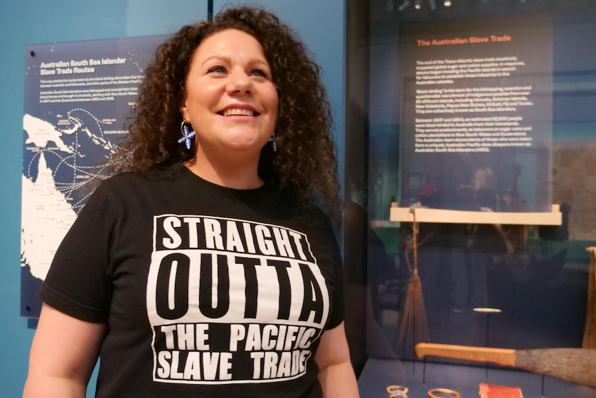 A South Sea Islander woman with long curly brown hair smiling wearing a statement tee "straight outta the pacific slave trade"