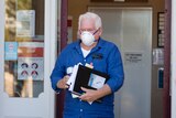 man wearing a mask and blue shirt holding documents