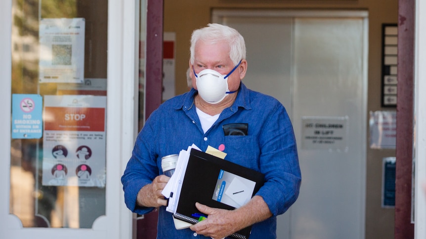 man wearing a mask and blue shirt holding documents