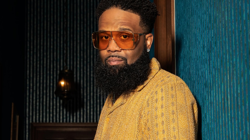Blanco Brown with beard wearing coloured glasses and a yellow shirt