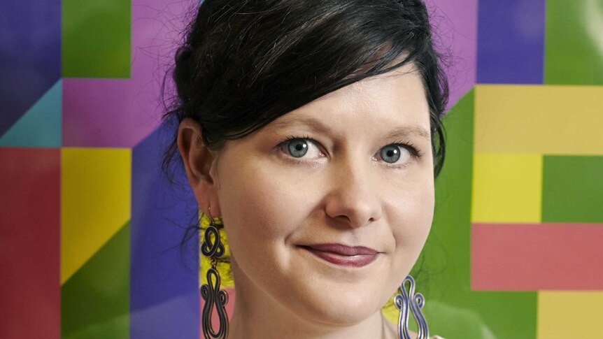 A portrait of a woman standing in front of a multicoloured backdrop.