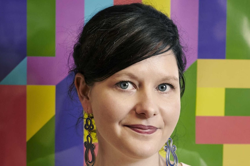 A portrait of a woman standing in front of a multicoloured backdrop.