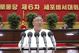 North Korean leader Kim Jong Un delivers a speech wearing white behind a row of microphones.