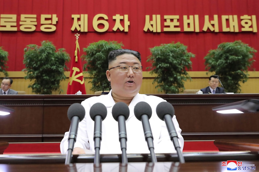 Pemimpin Korea Utara Kim Jong Un menyampaikan pidato dengan warna putih di belakang deretan mikrofon.