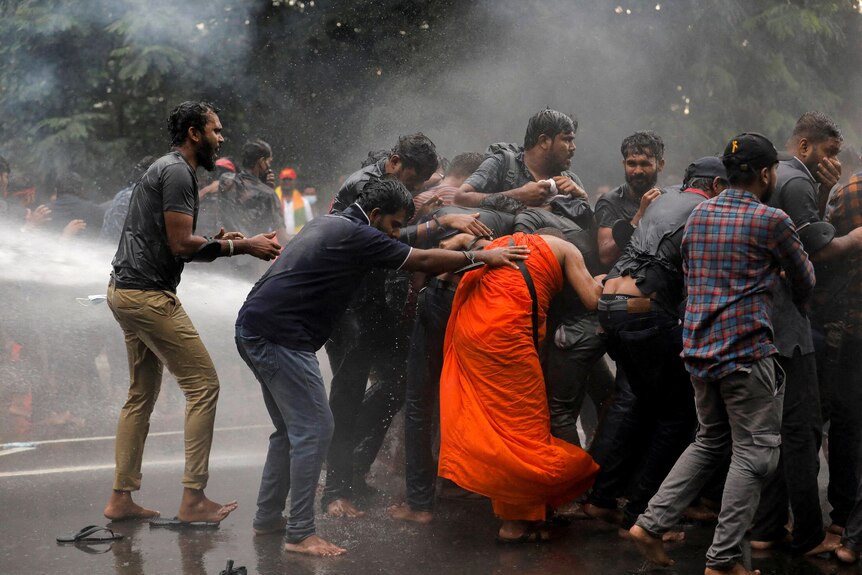 People crowd together as a jet of water is sprayed at them. One woman's orange dress is drenched