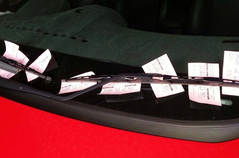 Red car's windscreen covered in parking tickets.