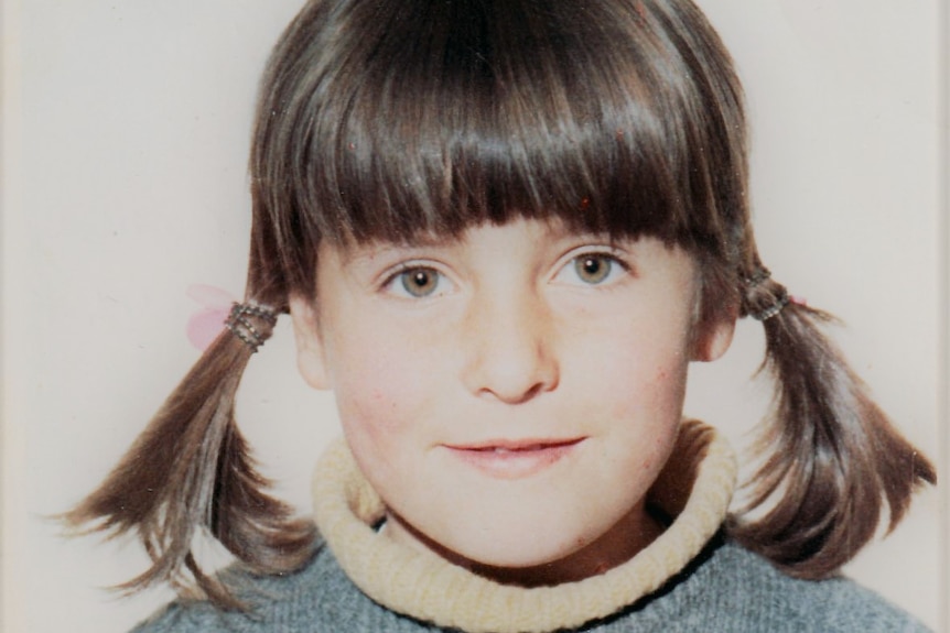 A portrait photo of a young girl in pigtails and grey knit top