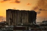 Firefighters extinguish a fire at the silos in the north block of the Beirut Port as the orange sun sets behind it