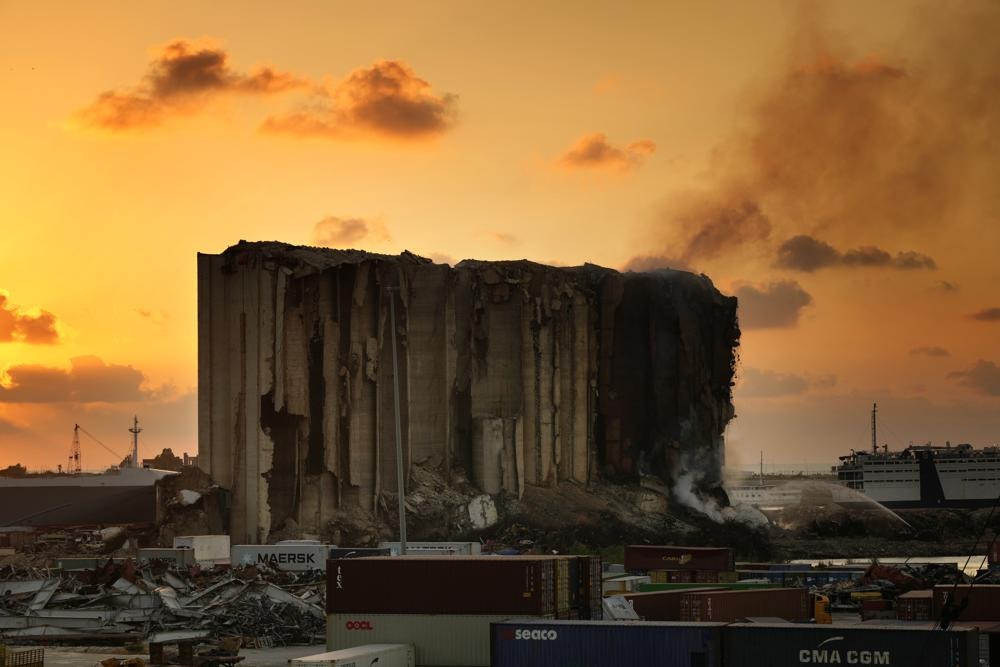 随着橙色的夕阳落下，消防员正在贝鲁特港口北区的筒仓中灭火在它后面